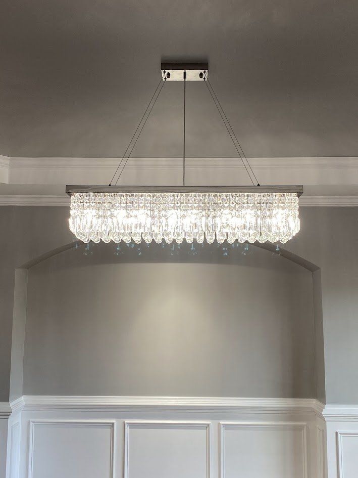 Linear crystal chandelier over a dining area with wainscoting