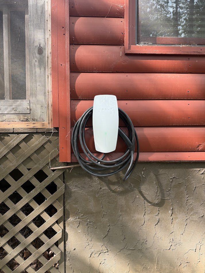 Tesla Wall Connector mounted on log siding with the cable neatly coiled