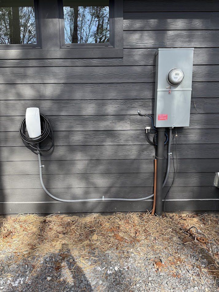 Tesla Wall Connector on dark siding, fed in flexible conduit from the meter base