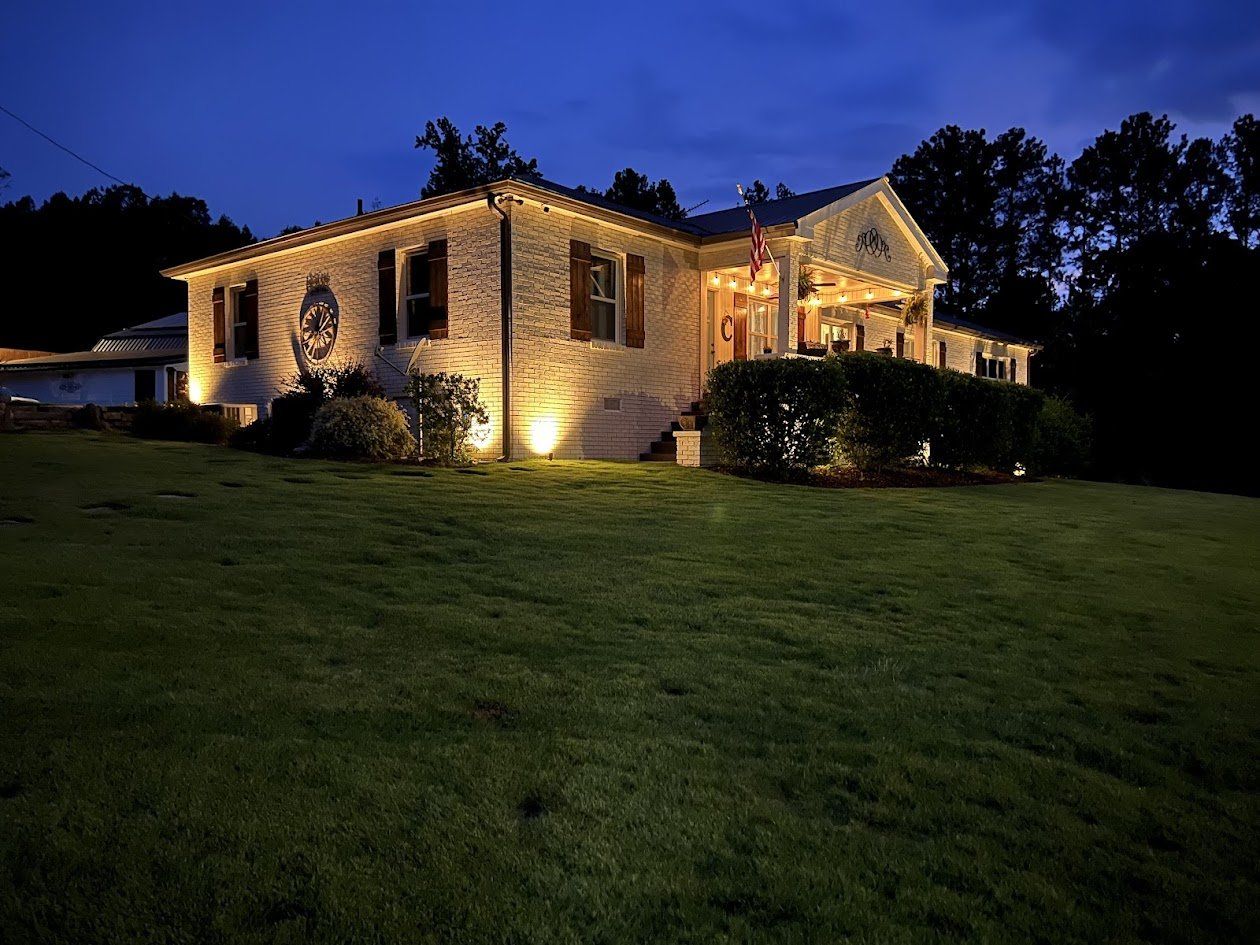 Corner view of a brick home with uplights along the walls and soffit lighting